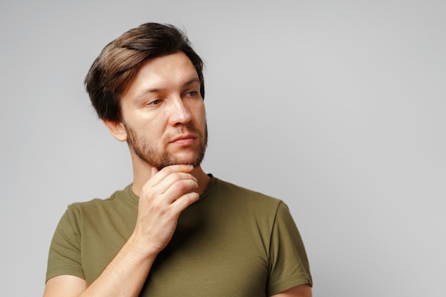 Portrait of a serious pensive young man against grey surface close up