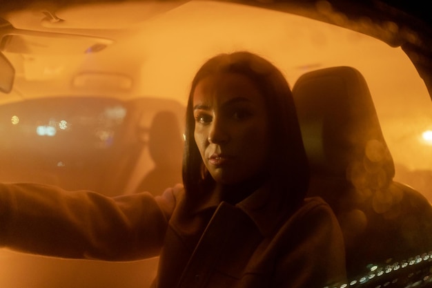 Portrait of serious relaxed woman enjoying night drive while sitting in car and looking at the