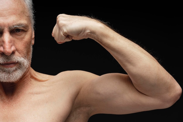 Portrait of serious retired mature man shirtless sportsman showing biceps muscular body