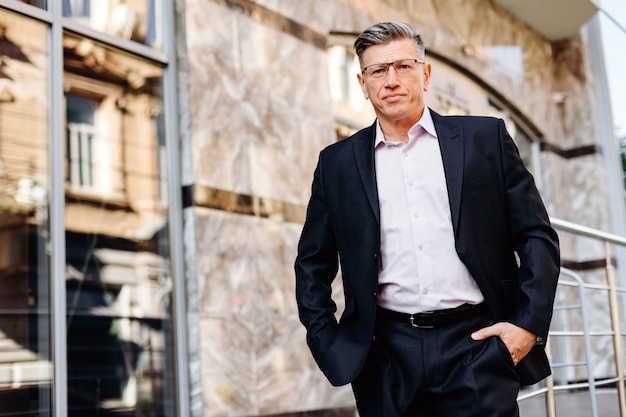 Portrait of serious senior man in suit standing outdoor . 