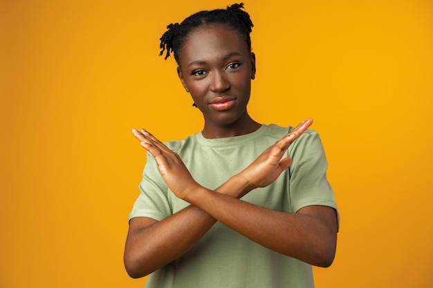 Portrait of a serious young african woman showing stop gesture in yellow studio