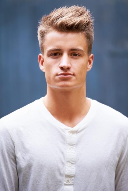 Portrait serious and young man with style on a wall background in the city Relax face and caucasian male person in a casual tshirt with trendy cool fashion from New Zealand with confidence