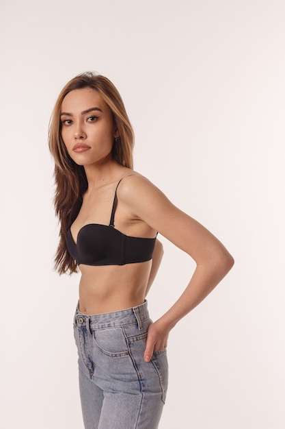 Portrait of sexy asian woman with long hair posing in black lingerie, blue jeans isolated on white