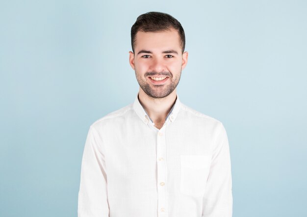 Portrait of sexy man in white casual shirt standing over blue background