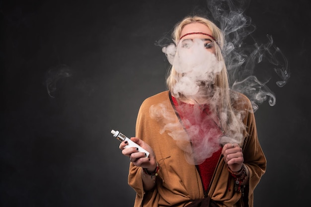 Portrait of sexy young hipster smoking vaping girl. The woman is dressed in the style of a boho. Vapor concept. Vaping e-Cigarette.