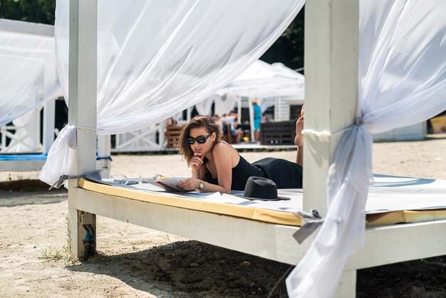 Photo portrait of sexy young woman wear black dress lying white beds gazebo near beach