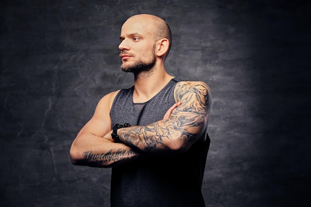 Portrait of shaved head athletic tattooed male with crossed arms over grey background.