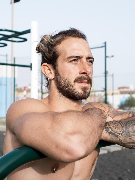 Portrait of a shirtless caucasian athlete with tattoos outdoor at the calisthenics park