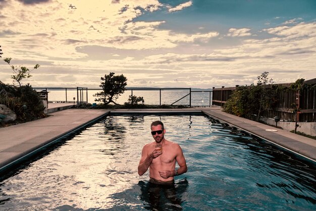 Portrait of shirtless man in swimming pool against sky