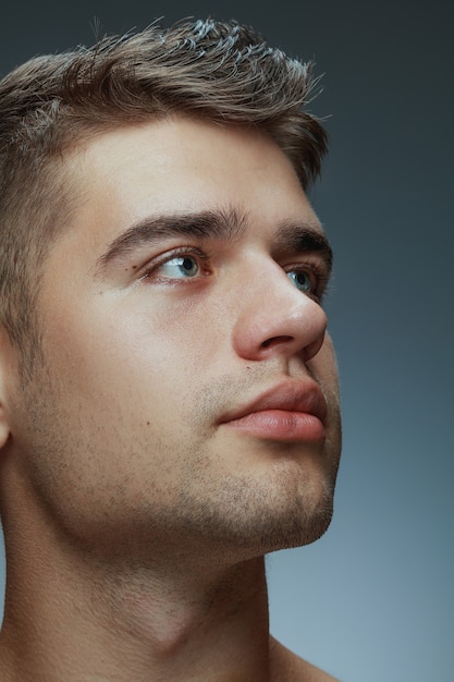 Portrait of shirtless young man isolated on grey studio background. Caucasian healthy male model looking at side and posing. Concept of men's health and beauty, self-care, body and skin care.