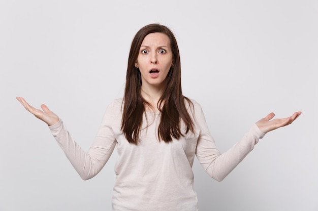 Portrait of shocked concerned young woman in light clothes spreading and pointing hands aside isolated on white background in studio. People sincere emotions, lifestyle concept. Mock up copy space.