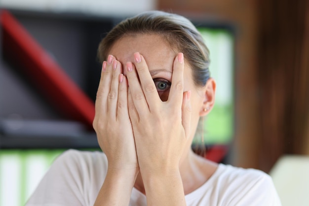 Portrait of shocked or scared woman looking through fingers female covering face with palms