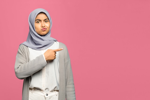 Portrait of shocked young Asian woman  pointing with finger to copy space