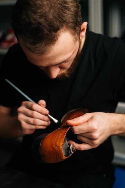 Portrait of shoemaker painting heel and sole of light brown leather shoes with brush