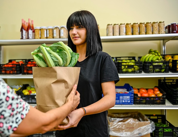 Portrait of shopman in the fruit store handing over a bag of fruit to a female customer