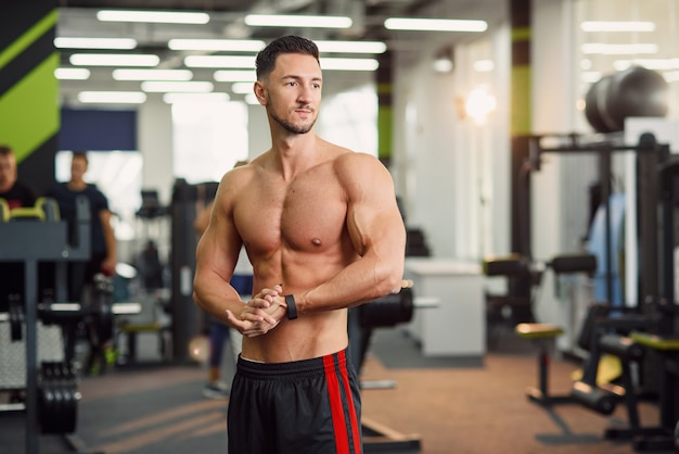 Portrait shot of attractive fitness guy with naked torso doing warm up exercises in the modern gym. Close up shot.