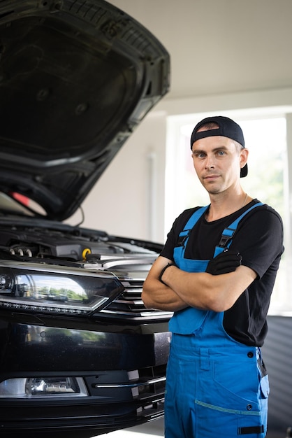 Portrait shot of caucasian man in blue uniform and hat standing in big auto garage looking to camera