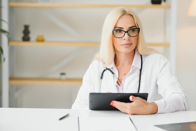 Portrait shot of middle aged female doctor sitting at desk and working in doctor office