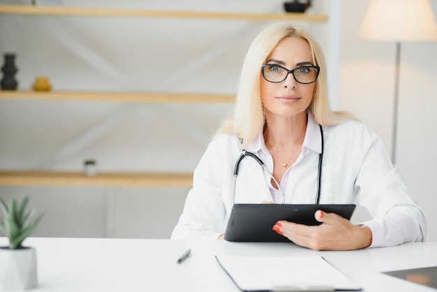 Portrait shot of middle aged female doctor sitting at desk and working in doctor office