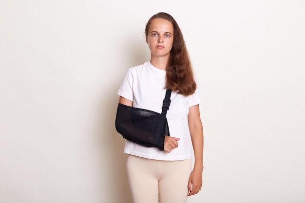 Portrait of sick arm broken Caucasian woman with arm sling supported on her hand being injured by accident and healthcare posing isolated on white background