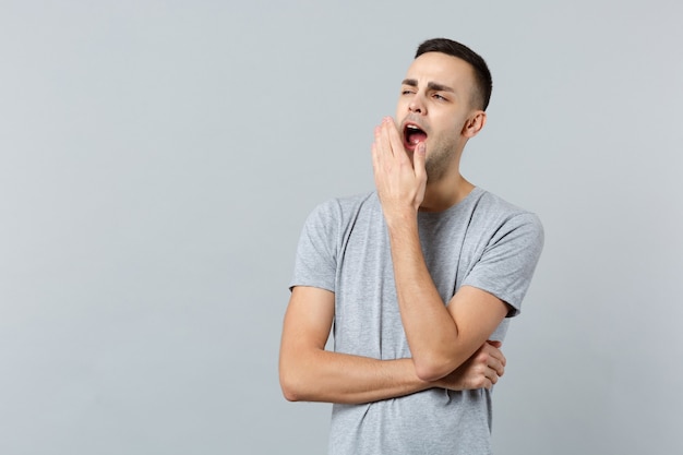 Portrait of sleepy young man in casual clothes looking aside yawning covering mouth with hand 