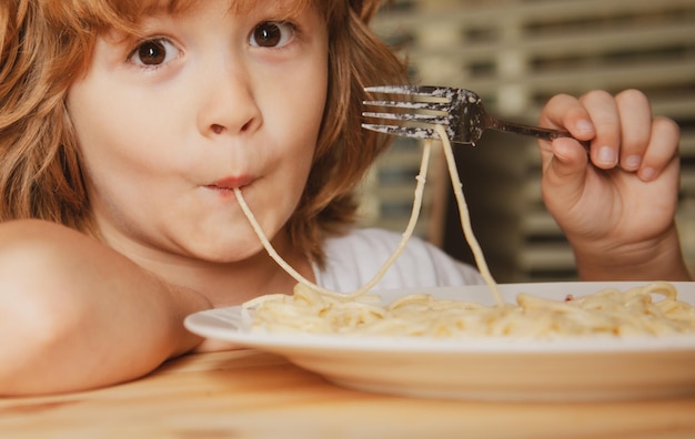 Portrait of a small blond boy eating pasta spaghetti closeup cute kids face positive emotional child