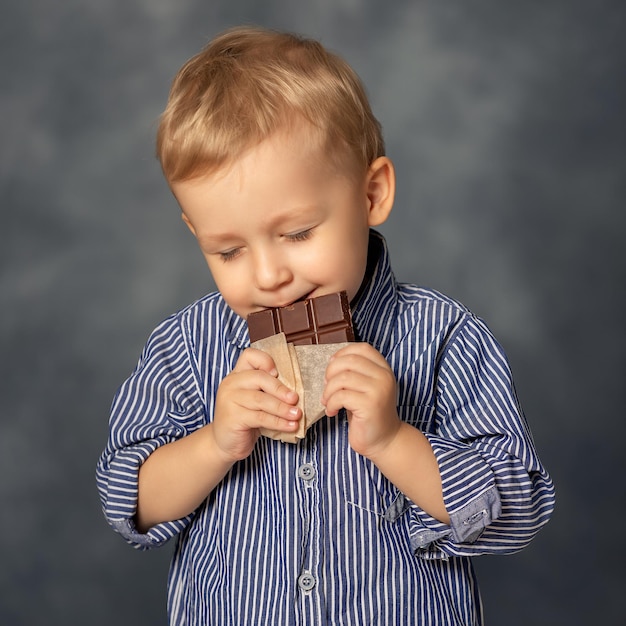 Portrait of small boy kid eating chocolate on grey background happy childhood concept sweet tooth