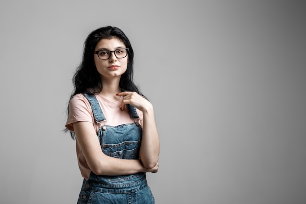 Portrait of smart beautiful brunette girl in eyeglasses with natural make-up, on grey background.