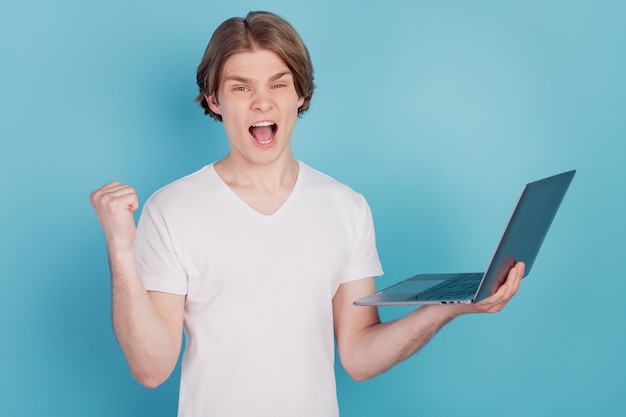 Portrait of smart guy holding laptop raise triumph fist isolated over blue background