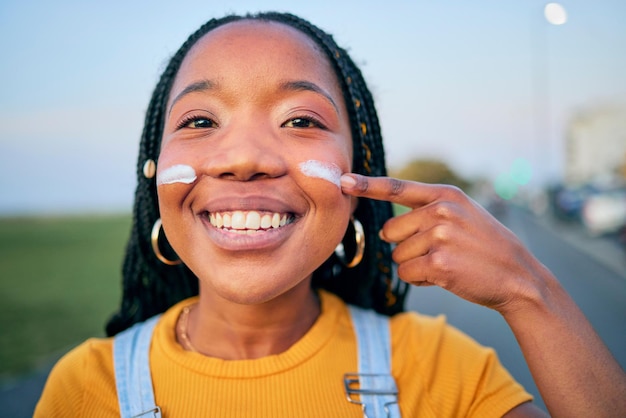 Portrait smile and a black woman with sunscreen on her face to protect her skin using spf treatment Summer street and blurred background with a happy young female person outdoor to apply lotion