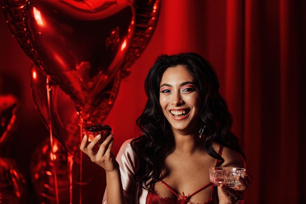 Portrait of smile sexy asian girl glam makeup in red lingerie with cupcake and glass of champagne