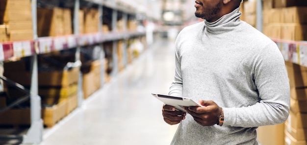 Portrait of smiling african american business man order details on tablet checking goods and supplies on shelves with goods background in warehouselogistic and business export