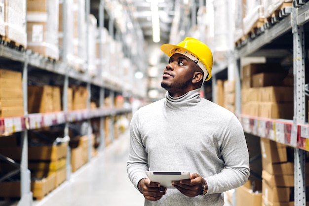 Portrait of smiling african american engineer man order details on tablet checking goods and supplies on shelves with goods background in warehouse.logistic and business export