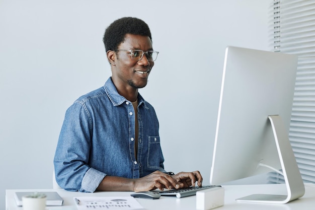 Portrait of smiling african american man working with pc at workplace in minimal office interior aga