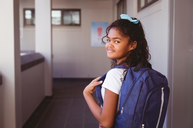 Portrait of smiling african american schoolgirl standing in school corridor wearing schoolbag