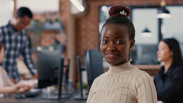 Portrait of smiling african american software developer looking at camera in artificial intelligence development agency. Confident programer posing next to colleagues working in big data office.