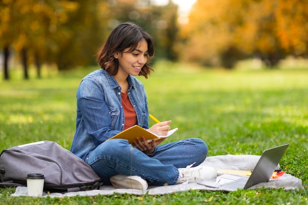 Portrait Of Smiling Arab Female Student Preparing For Exam With Computer Outdoors