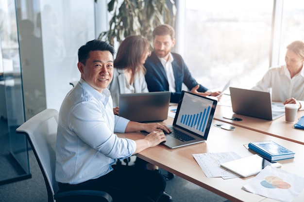 Portrait of smiling asian businessman working on a laptop during a meeting with a team