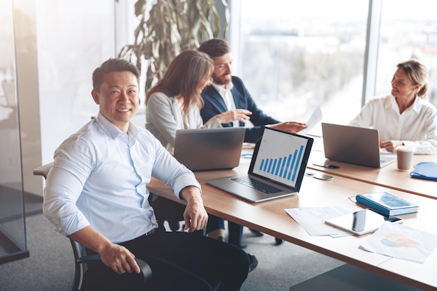 Portrait of smiling asian businessman working on a laptop during a meeting with a team