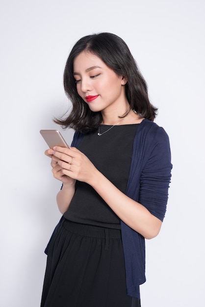 Portrait of a smiling asian casual woman holding smartphone over white background