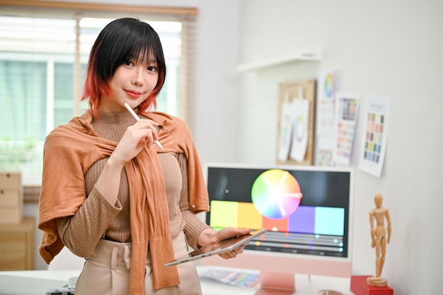 Portrait of a smiling Asian female web graphic designer stands in her studio