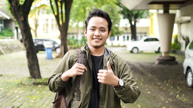 Portrait of a smiling Asian man wearing a bag with ok gesture