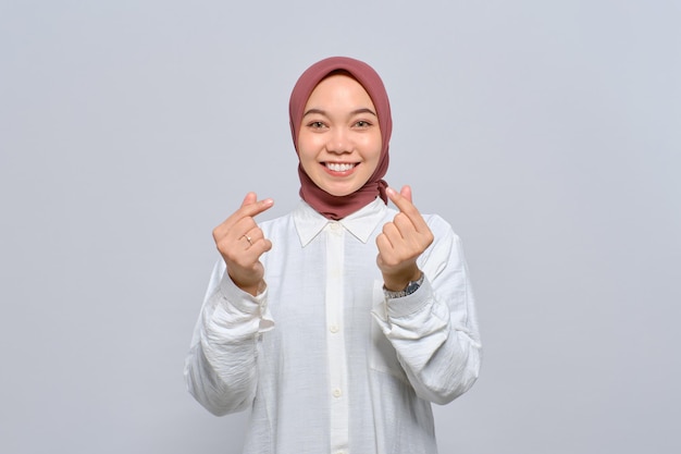 Portrait of smiling Asian Muslim woman showing Korean heart gesture isolated over white background