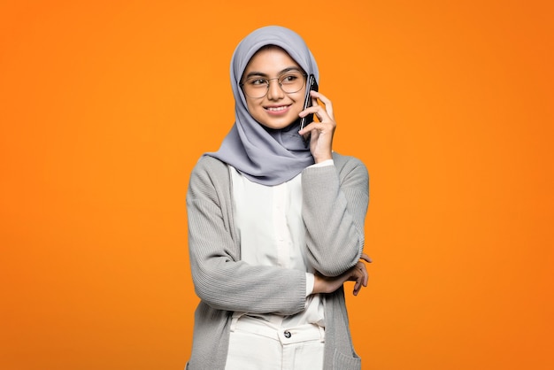 Portrait of smiling beautiful Asian woman while talking with friend at smartphone