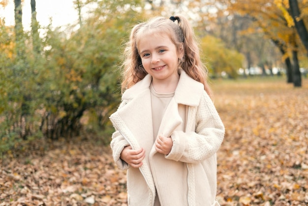 portrait of smiling beautiful little girl in stylish clothes in nature in autumn park