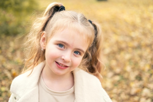 portrait of smiling beautiful little girl in stylish clothes in nature in autumn park