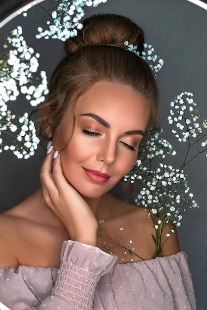 Portrait of a smiling beautiful sweet girl on a gray background with white flowers