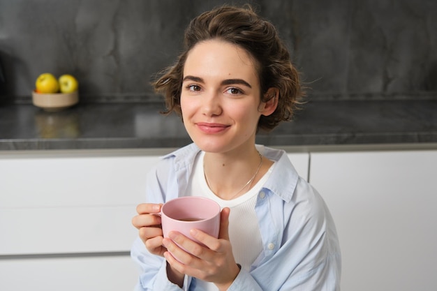 Portrait of smiling beautiful young woman drinking coffee in kitchen morning magic with cuppa tea lo