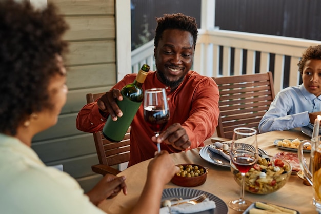 Portrait of smiling black man pouring wine to glasses while enjoying dinner party outdoors