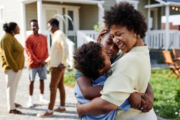 Portrait of smiling black woman embracing two sons at family gathering outdoors copy space